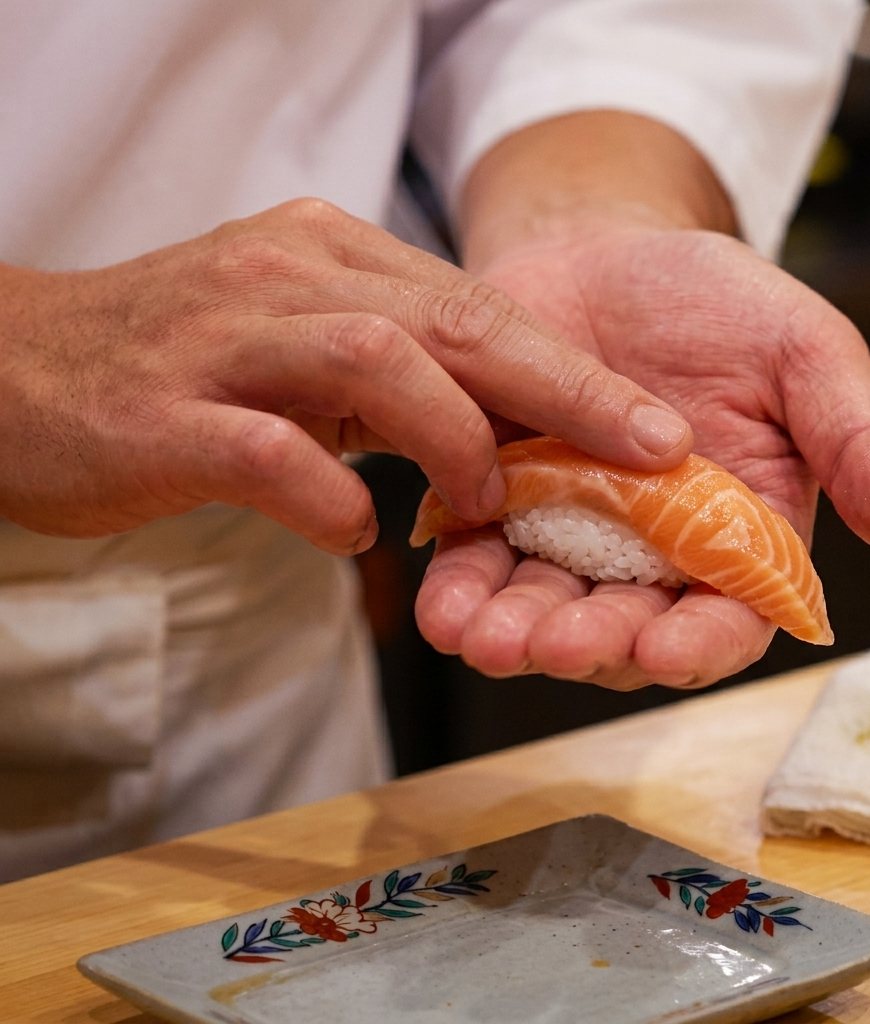 A sushi chef holding a freshly pressed salmon nigiri